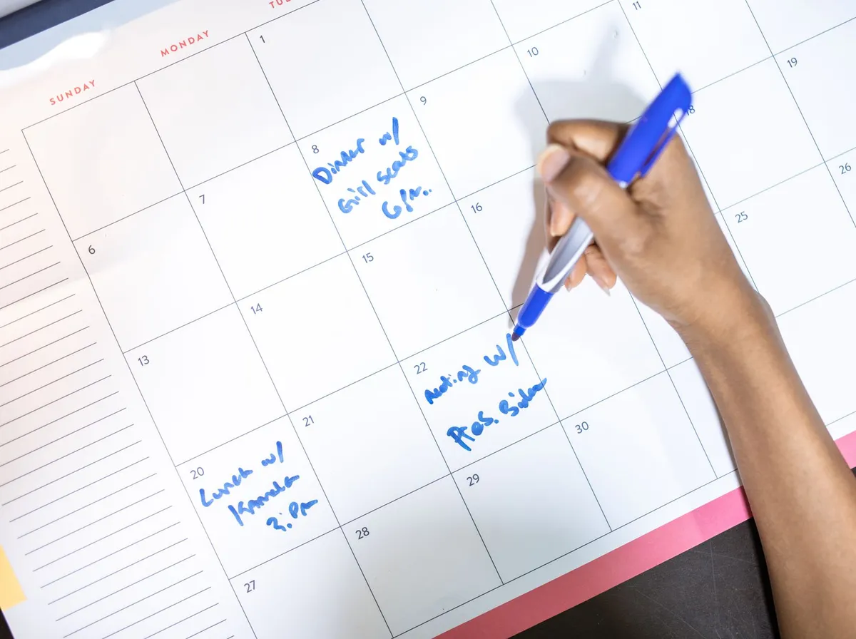 Main qui note des rendez-vous sur un calendrier mensuel papier, planification d'une cadence de publication régulière